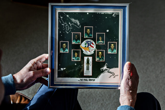 Brian Russell holds a picture that hangs on a wall at his home that memorializes the astronauts killed in the Challenger explosion.