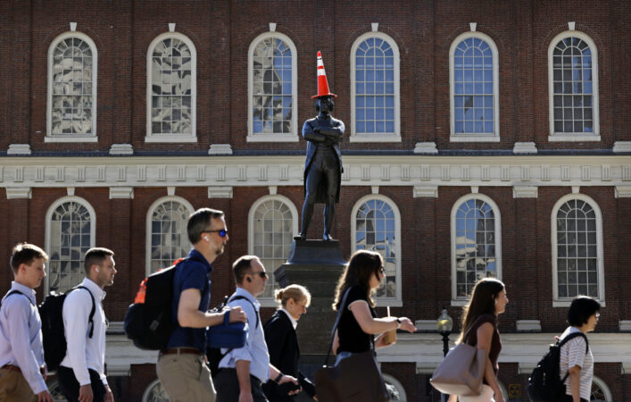 A traffic cone sits atop the statue of Samuel Adams as morning commuters pass Faneuil Hall in Boston, MA on June 17, 2026.