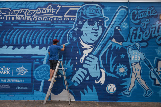 Paul Carpenter works on his mural at 20th Street and Oregon Avenue on Thursday. Carpenter created the artwork for Deer Park's limited-edition water bottles and is scaling it for a South Philly wall.