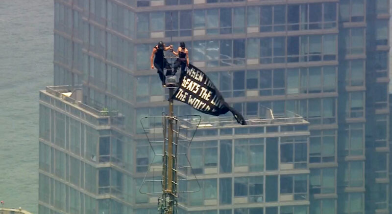 Two people stand on the tip of the antenna of the Empire State Building in New York while holding a banner on Wednesday, July 1, 2026.