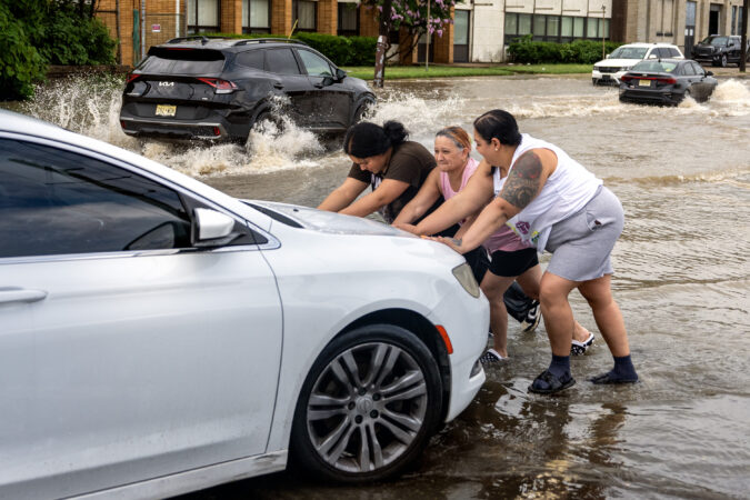 Husband Omar Marquez is behind the wheel as Angie Colon gets help from her mother and daughter pushing their car after it stalled while driving through high water on Ferry Avenue near PATCO station, the White Horse Pike and Route 130 in Camden Monday, July 6, 2026, as a flash flood threat continues for the region. The family was trying to get home nearby from shopping.