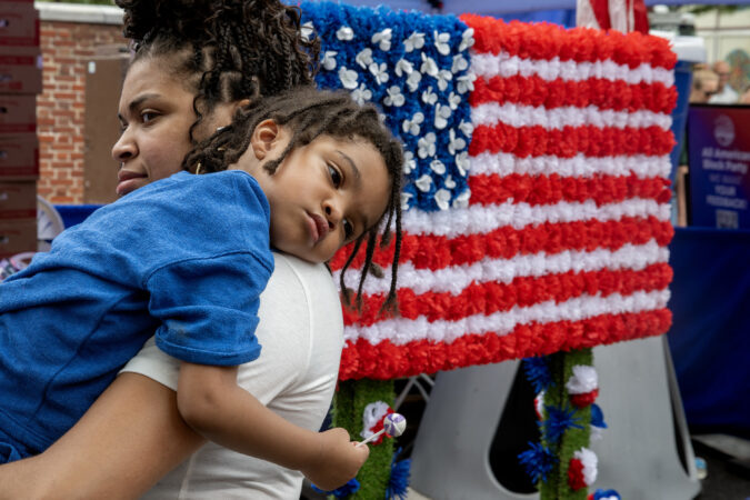Ciera Brown carries her son, Asaad Neely, 3, as they march in the second annual Red, White, & Blue To-Do parade Wednesday, Jul, 2, 2025, along with whimsical red wagon floats, marching bands, John Adams and Ben Franklin, and representatives from over twenty groups across Philadelphia’s Historic District. The event commemorates a day of “pomp and parade,” as declared by John Adams in 1776. He believed Independence Day would be celebrated on the 2nd - when the Continental Congress officially voted for independence - not two days later when he, John Hancock (and 54 others) signed their document,